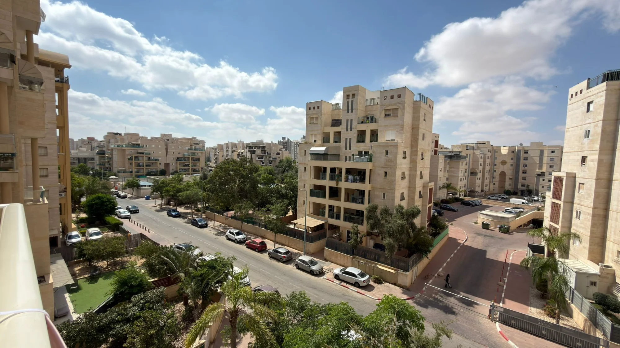 נוף עירוני של בנייני מגורים בבאר שבע, עם רחוב ושדרת עצים, תחת שמיים כחולים ועננים