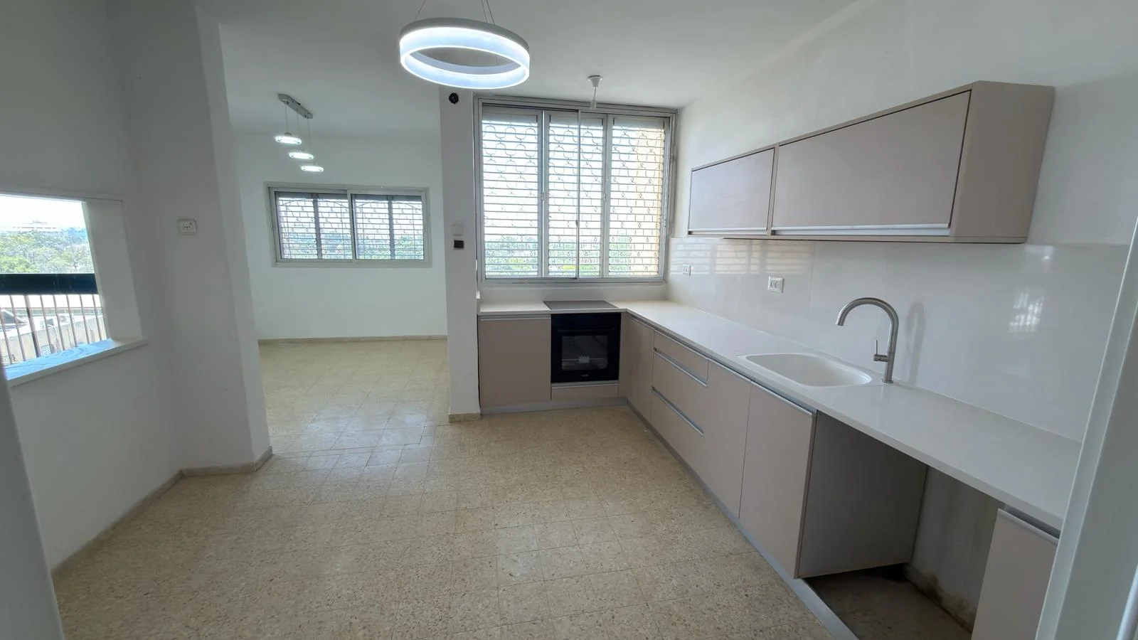 מטבח מודרני בדירה, עם ארונות בהירים, משטח עבודה לבן וכיריים