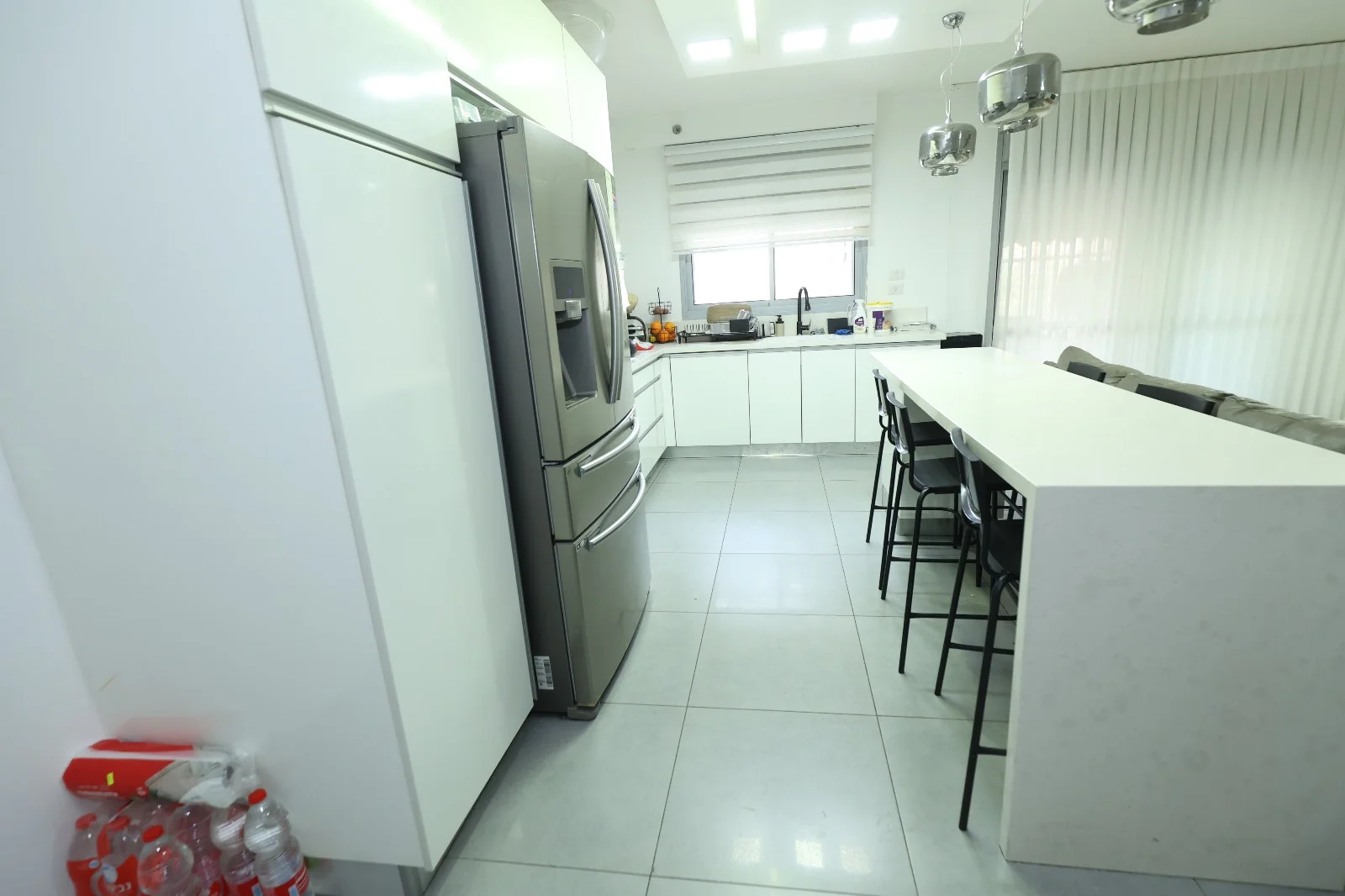 מטבח מודרני ופתוח עם ארונות לבנים, מקרר נירוסטה, ואי עם כיסאות בר