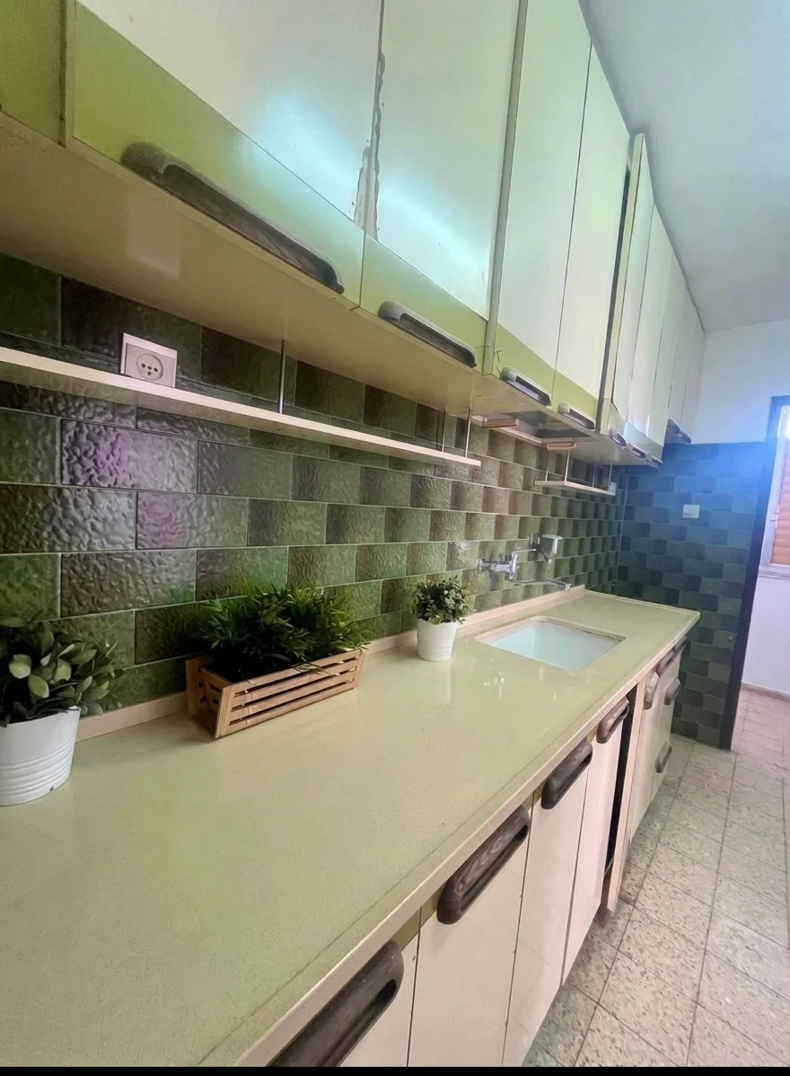 מטבח עם ארונות ירוקים, משטח עבודה בהיר וכיור, וקיר מצופה באריחים ירוקים.